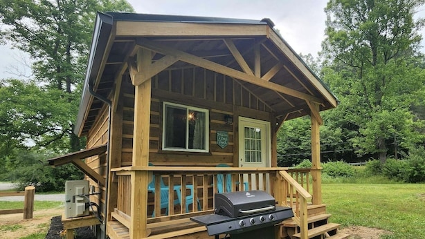 Una baita di legno con veranda, barbecue e un cartello con scritto 'Welcome Back'.
