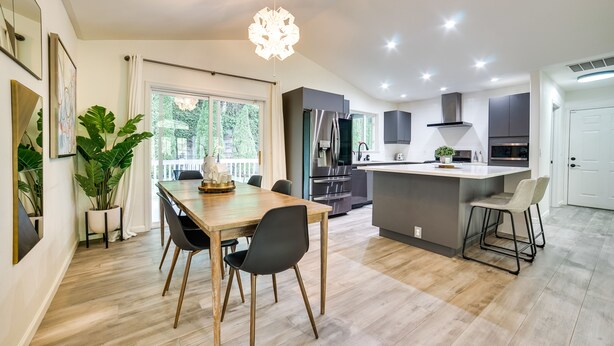 Eine moderne Küche mit einer zentralen Kochinsel, Edelstahlgeräten und einem Essbereich mit Holztisch und Stühlen.