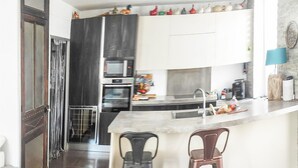 A modern kitchen with dark cabinetry, a built-in oven, a microwave, and a sink. There are two stools at the counter and a decorative birdcage on the wall.