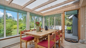 A conservatory with a wooden table and chairs, large windows, and a view of greenery. - Lovely home in Hemmet with WiFi (Hemmet)