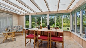 A covered patio with a wooden table and chairs, large windows, and a view of greenery. - Lovely home in Hemmet with WiFi (Hemmet)