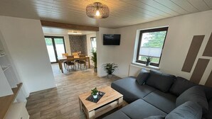 Ein modernes Wohnzimmer mit einem grauen Ecksofa, einem Couchtisch aus Holz und einem an der Wand montierten Fernseher.