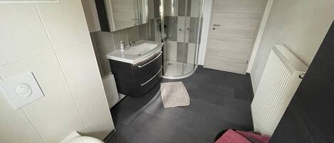 Et moderne badeværelse med toilet, håndvask og bruseområde.