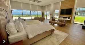 Relax in a spacious room with a large bed and a flat-screen TV, offering a view of the outdoors through a large window.