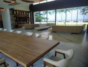 Relax in a spacious living area with a large dining table and comfortable seating, offering a view of palm trees and the beach.
