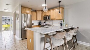 A modern kitchen with wooden cabinets, a marble island, and bar stools. - SunnySide Up ~ Beach & Bay!! (Pensacola Beach)