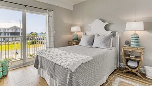 A bedroom with a large bed, two bedside tables with lamps, a view of the outside, and a balcony. - SunnySide Up ~ Beach & Bay!! (Pensacola Beach)
