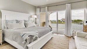 A bedroom with a large bed, a nightstand, a dresser, and a view of a body of water through large windows. - SunnySide Up ~ Beach & Bay!! (Pensacola Beach)