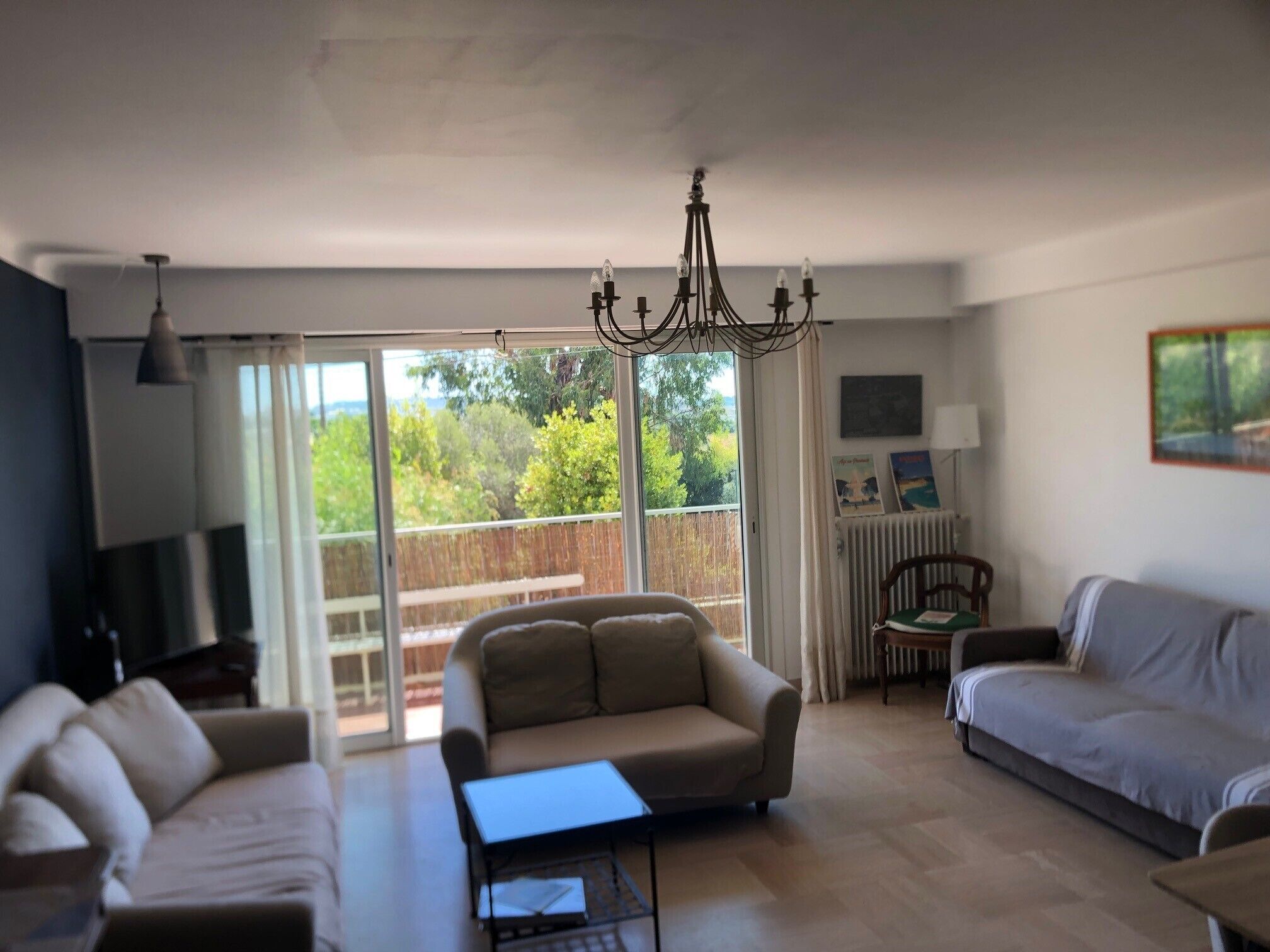 A spacious living room with a large sliding glass door leading to a balcony, a chandelier, and a cozy seating area with a sofa and armchairs.