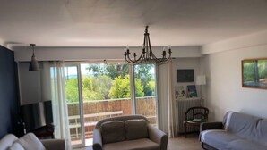 Amplia sala de estar con un gran ventanal corredero que da a un balcón, un candelabro y una zona de estar acogedora con sofá y sillones.