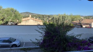 Vista desde un balcón sobre un estacionamiento con coches, un edificio de techo de tejas y una colina al fondo.