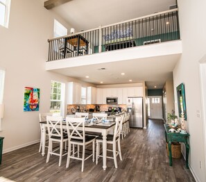 A spacious kitchen with white cabinetry, a dining area with white chairs, and a balcony with a railing.