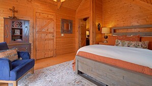 A wooden cabin bedroom with a bed, a blue sofa, a wooden cabinet, and a door. - 4D Guest Ranch~Large private pool with volley ball and basket ball nets (Waelder)