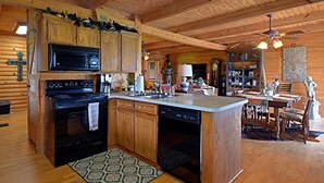 A wooden cabin interior with a kitchen featuring a stove, microwave, and dishwasher, a dining area with a table and chairs, and a ceiling fan. - 4D Guest Ranch~Large private pool with volley ball and basket ball nets (Waelder)