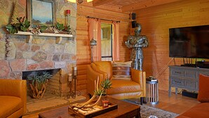 A cozy log cabin interior with a stone fireplace, leather sofa, and a television. - 4D Guest Ranch~Large private pool with volley ball and basket ball nets (Waelder)