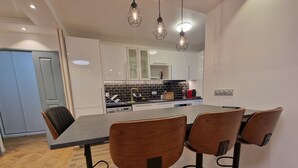 Een moderne keuken met witte kasten, een zwarte spatwand en een centraal eiland. Rond een rechthoekige tafel staan vier houten stoelen met zwarte metalen poten.