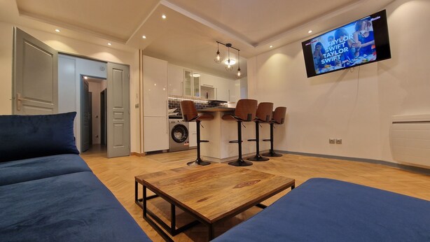 Een moderne woonkamer met een bank, een houten salontafel en een aan de muur bevestigde televisie.