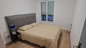 Een slaapkamer met een bed, een nachtkastje met lamp, een raam met zonwering en een plafondlamp.