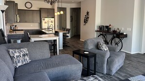 Moderni olohuone, jossa on harmaita sohvia, sohvapöytä ja ruokailutila. Taustalla näkyy keittiö.