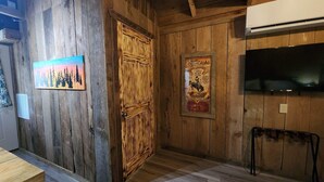 Un interior rústico de madera con una puerta de madera, un cartel enmarco, un televisor montado y un banco de madera.