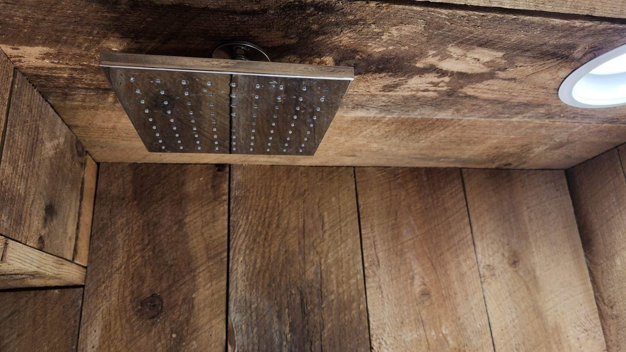A shower area with a metal showerhead and wooden walls.