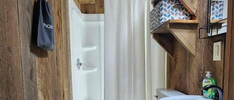 Un baño rústico con paredes de madera, un inodoro blanco, un lavamanos con espejo y una cortina de ducha.