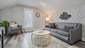 Ein modernes Wohnzimmer mit grauem Sofa, rundem Couchtisch und Wandpapier mit Muster.
