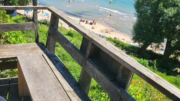 Eine Holzterrasse mit Blick auf einen Strand, wo Menschen schwimmen und sonnenbaden.