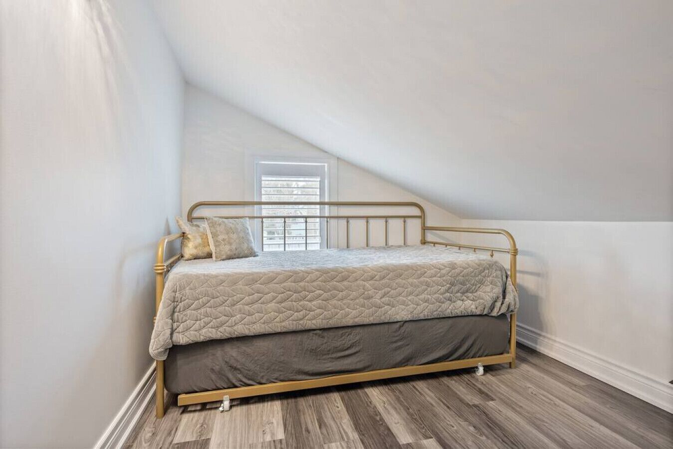 Una cama individual en una habitación con techos inclinados y suelo de madera.