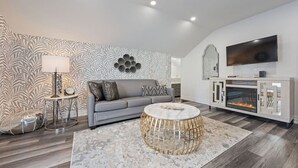 Ein modernes Wohnzimmer mit einem grauen Sofa, einem runden Couchtisch, einem Kamin und einem an der Wand montierten Fernseher.