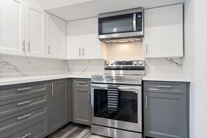 A modern kitchen with grey cabinets, a stainless steel oven, and a microwave above it.