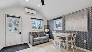 A compact living space with a grey sofa, a dining table with chairs, and patterned wallpaper. - Luxe Lodges on Lake Erie ~ Bunkie ~ Beach Access (Port Dover)