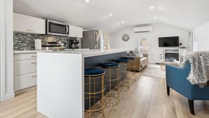 A modern kitchen with a central island, bar stools, a sofa, and a TV in a living area.