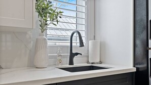 A kitchen with a black faucet, a white vase, a bottle of hand soap, and a paper towel holder. - Luxe Lodges on Lake Erie ~ Emerald ~ Beach + Patio (Port Dover)
