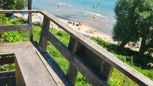 A wooden deck overlooking a beach with people swimming and sunbathing. - Luxe Lodges on Lake Erie ~ Emerald ~ Beach + Patio (Port Dover)
