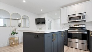 A modern kitchen with dark cabinets, stainless steel appliances, and a white countertop. - Luxe Lodges on Lake Erie ~ Emerald ~ Beach + Patio (Port Dover)