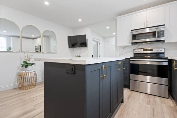 A modern kitchen with dark cabinets, stainless steel appliances, and a white countertop.
