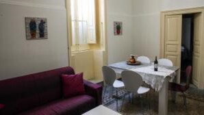 A small dining area with a table and chairs, a window with blinds, and a door leading to another room. - PALAZZO NICASTRO gh - Red House apartment (Avola)