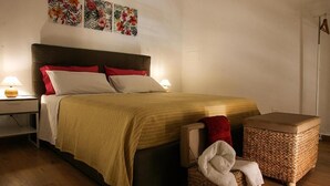 A bedroom with a bed, bedside tables, a nightstand, a woven basket, and a wall with floral artwork. - PALAZZO NICASTRO gh - Red House apartment (Avola)