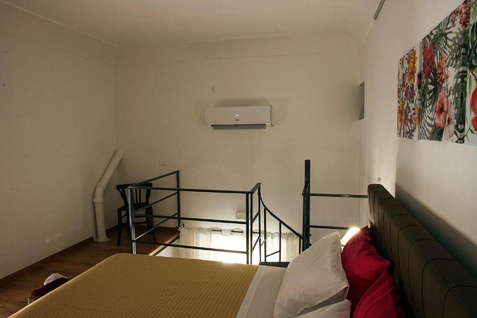 A room with a bed, a staircase, a wall-mounted air conditioner, and a floral painting.