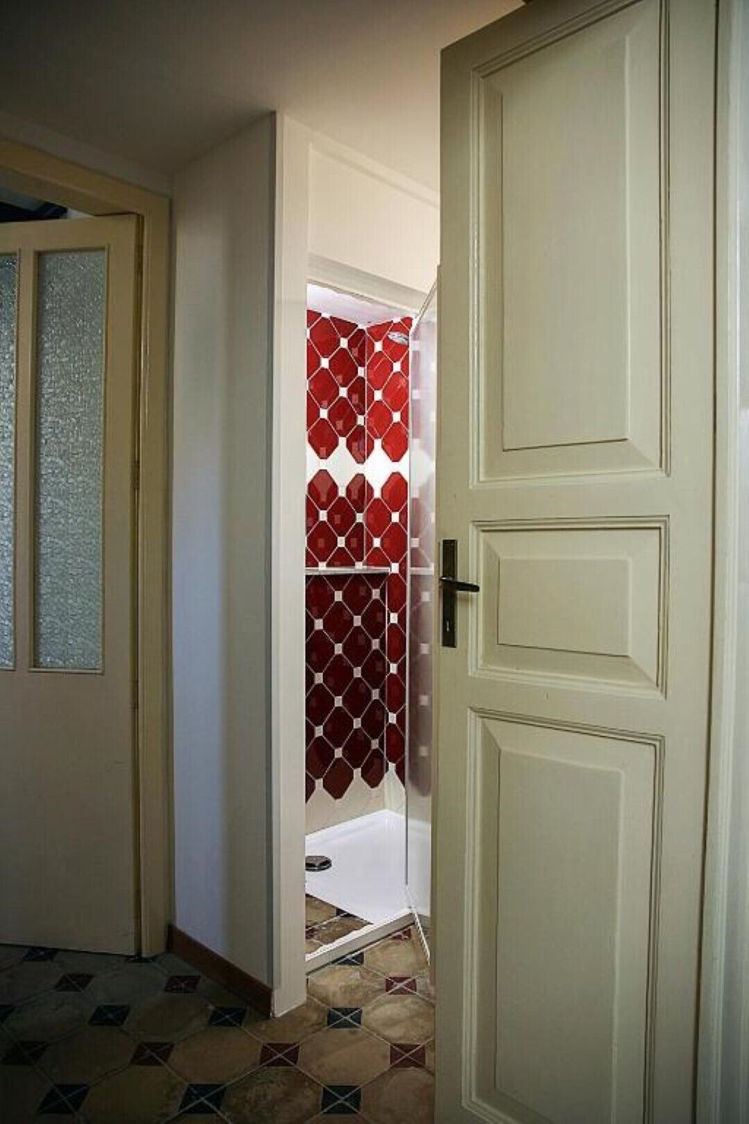 A hallway with a tiled floor, a door with a glass panel, and a red patterned door.
