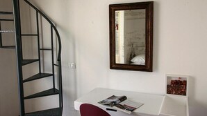 A room with a white desk, a red chair, a spiral staircase, and a mirror on the wall. - PALAZZO NICASTRO gh - Red House apartment (Avola)