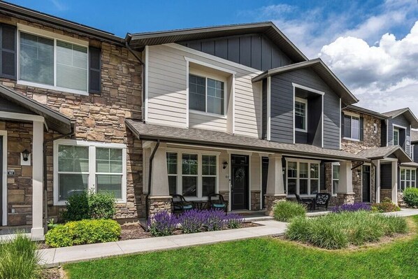 A row of townhouses with stone facades, multiple windows, and a front porch with outdoor seating. - Spacious 2-Story, Pet&Fam Friendly, WFH, Gym&Pool (Draper)