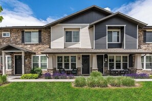 A two-story house with a stone facade, a covered front porch with outdoor seating, and a well-maintained lawn. - Spacious 2-Story, Pet&Fam Friendly, WFH, Gym&Pool (Draper)