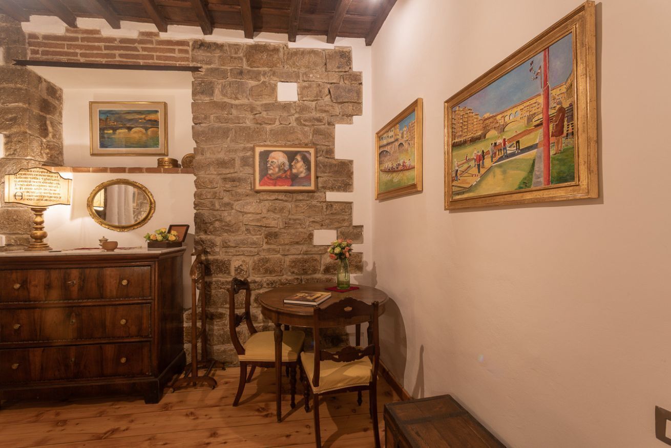 A room with a stone wall, wooden furniture, a round table with chairs, and paintings on the wall.