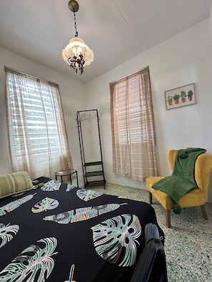 Une chambre à coucher comprenant un lit, une chaise, une étagère et une fenêtre avec des rideaux.