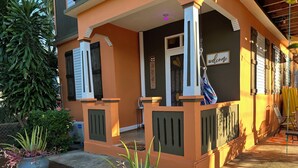 Ein Gebäude mit Veranda, Tür und Fenster. Auf dem Boden stehen Pflanzen in Töpfen.