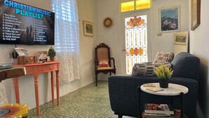 Ein gemütliches Wohnzimmer mit einem hölzernen Beistelltisch, einem blauen Sofa und einem an der Wand montierten Fernseher, der eine Playlist christlicher Musik zeigt.