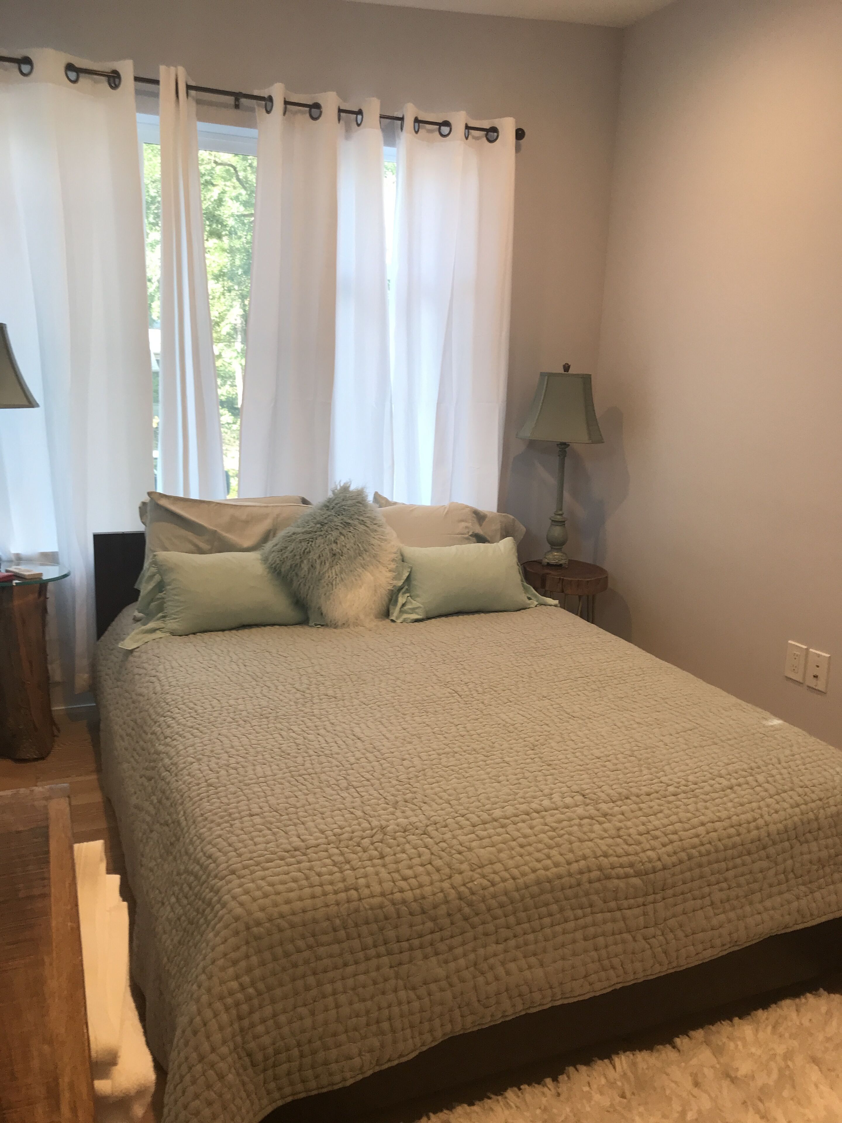 Ein Schlafzimmer mit Bett, Vorhängen, einer Lampe und einem Fenster.