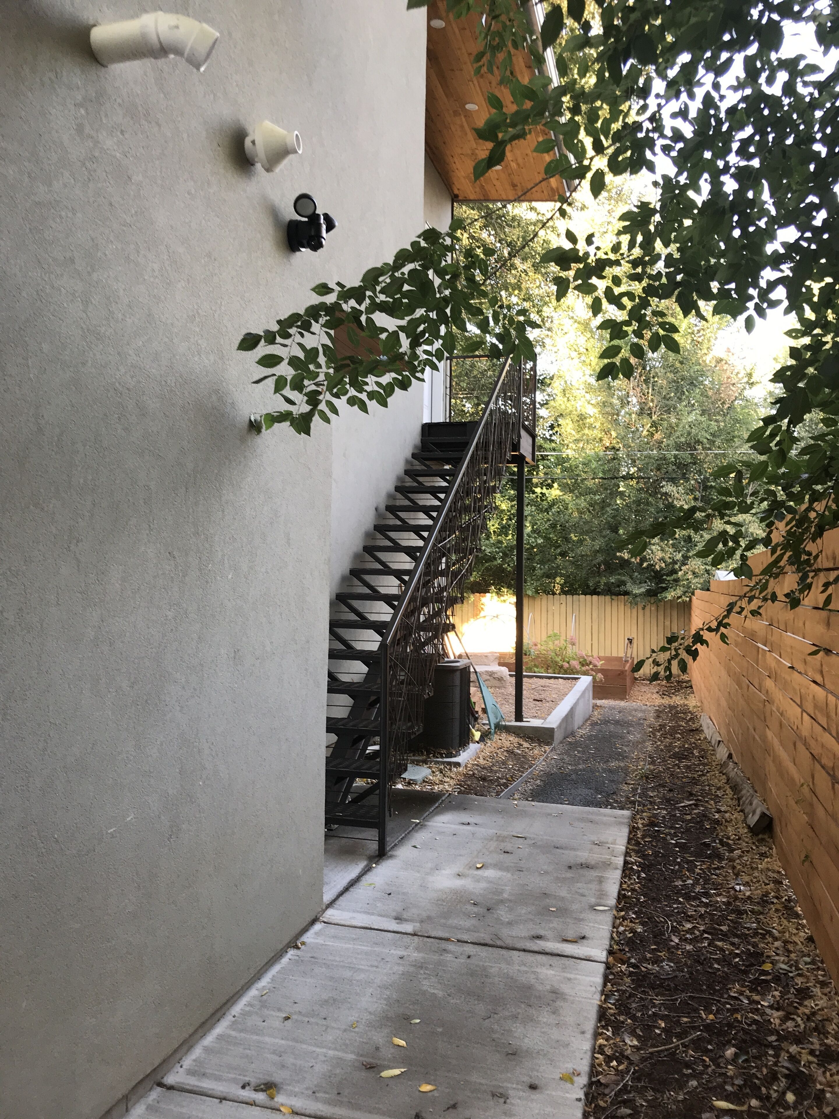 Eine Betontreppe führt zu einer Holzterrasse, umgeben von einem Garten mit Mulch und einem Holzzaun.